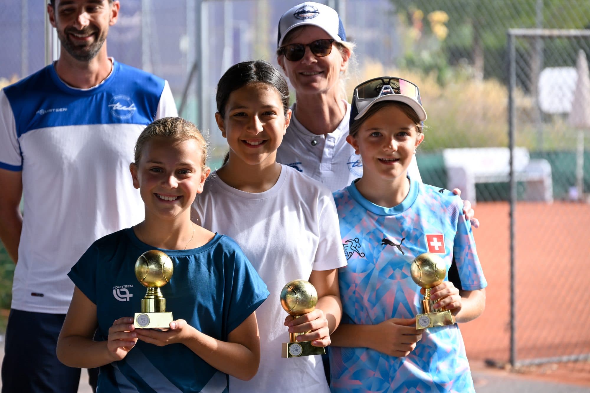 Trois jeunes joueuses fières de leur petit trophée doré, entourées des coachs